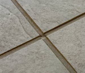 Close-up of low grout joints in a porcelain tile floor showing recessed grout below the tile edges and exposed tile sidewalls.