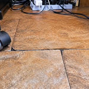 Illustrative image showing an office chair caster adjacent to damaged LVT/SPC flooring with chipped edges, joint separation, and rolling-load related wear.